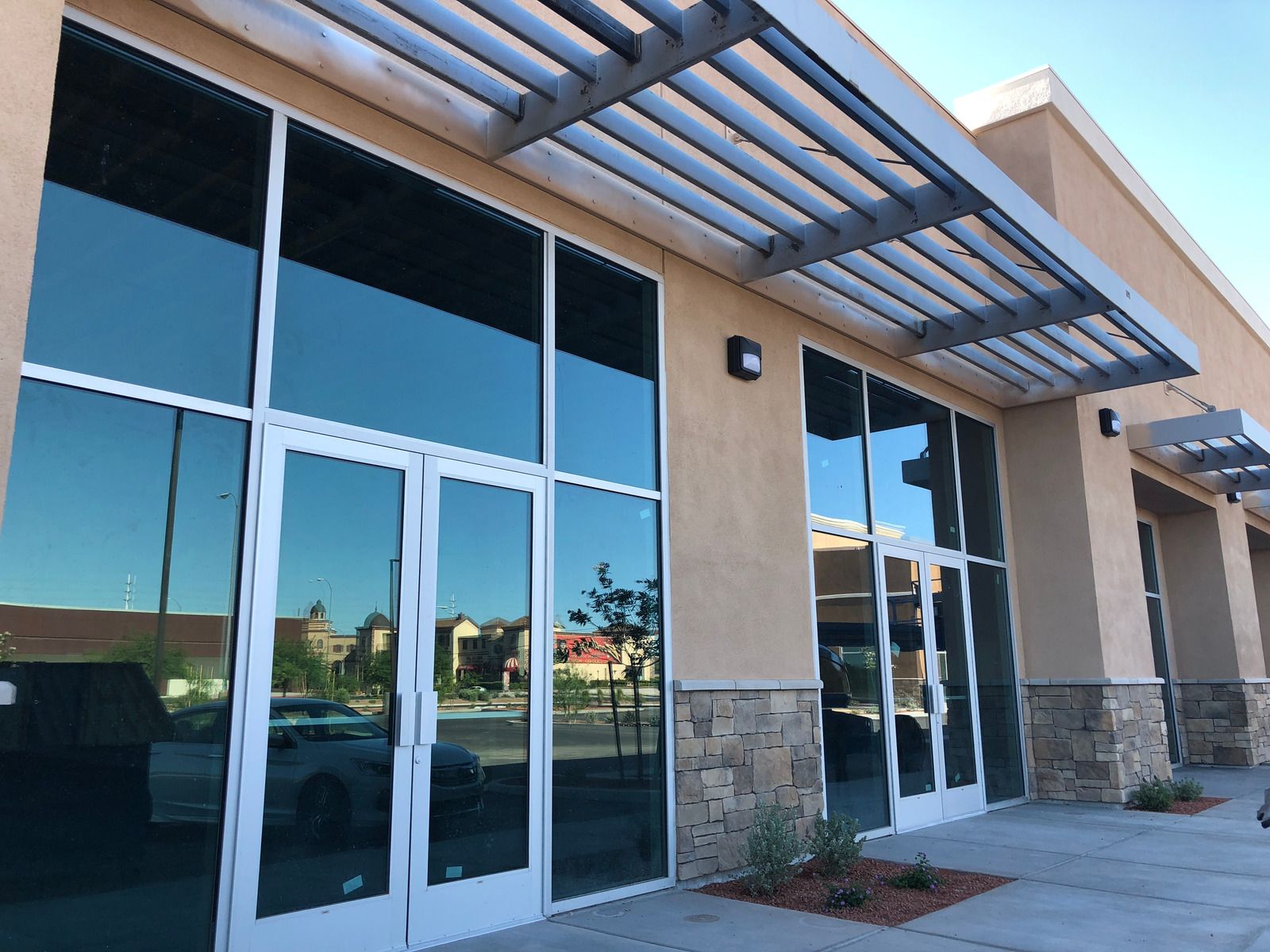 Exterior of a building with large reflective windows, a metal awning, and beige stucco walls.