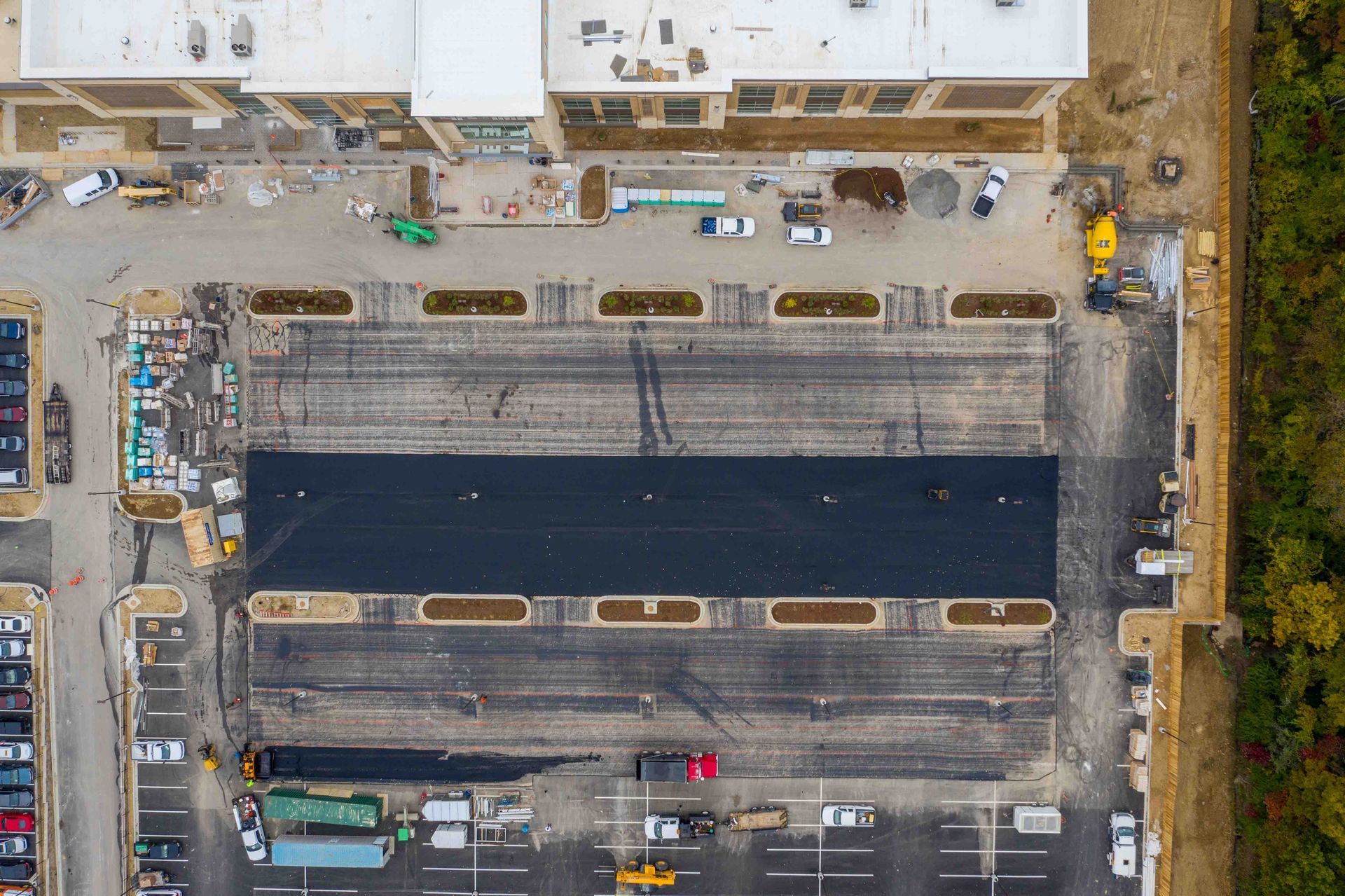 Overhead view of parking lot construction with fresh asphalt, surrounded by partially completed landscaping and buildings.