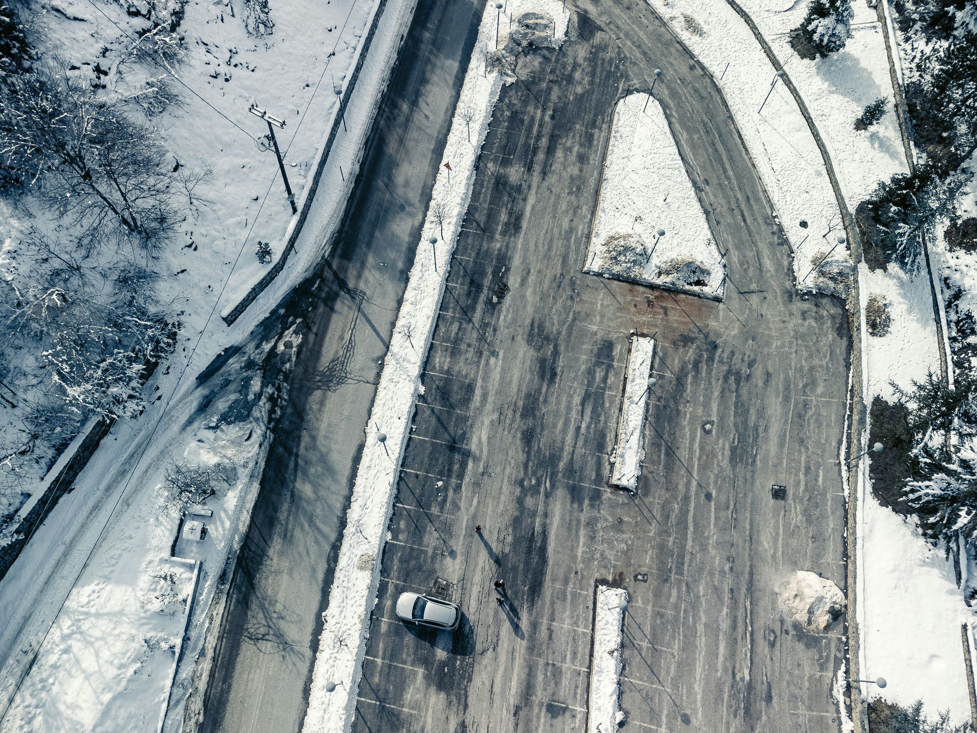 An aerial view of a snow-covered road with a single car driving.