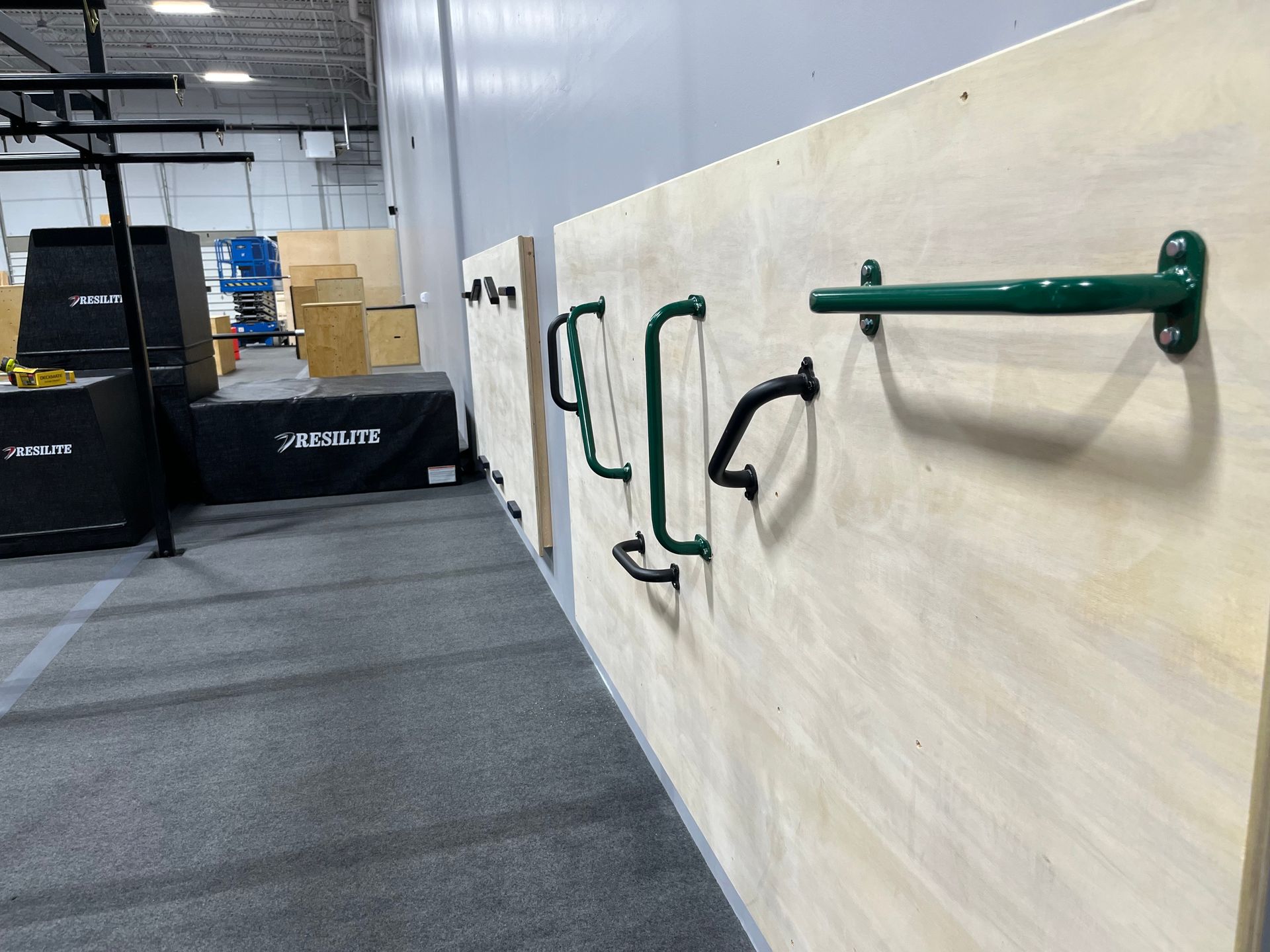 Green and black climbing handholds on a light wooden wall in an indoor gym.