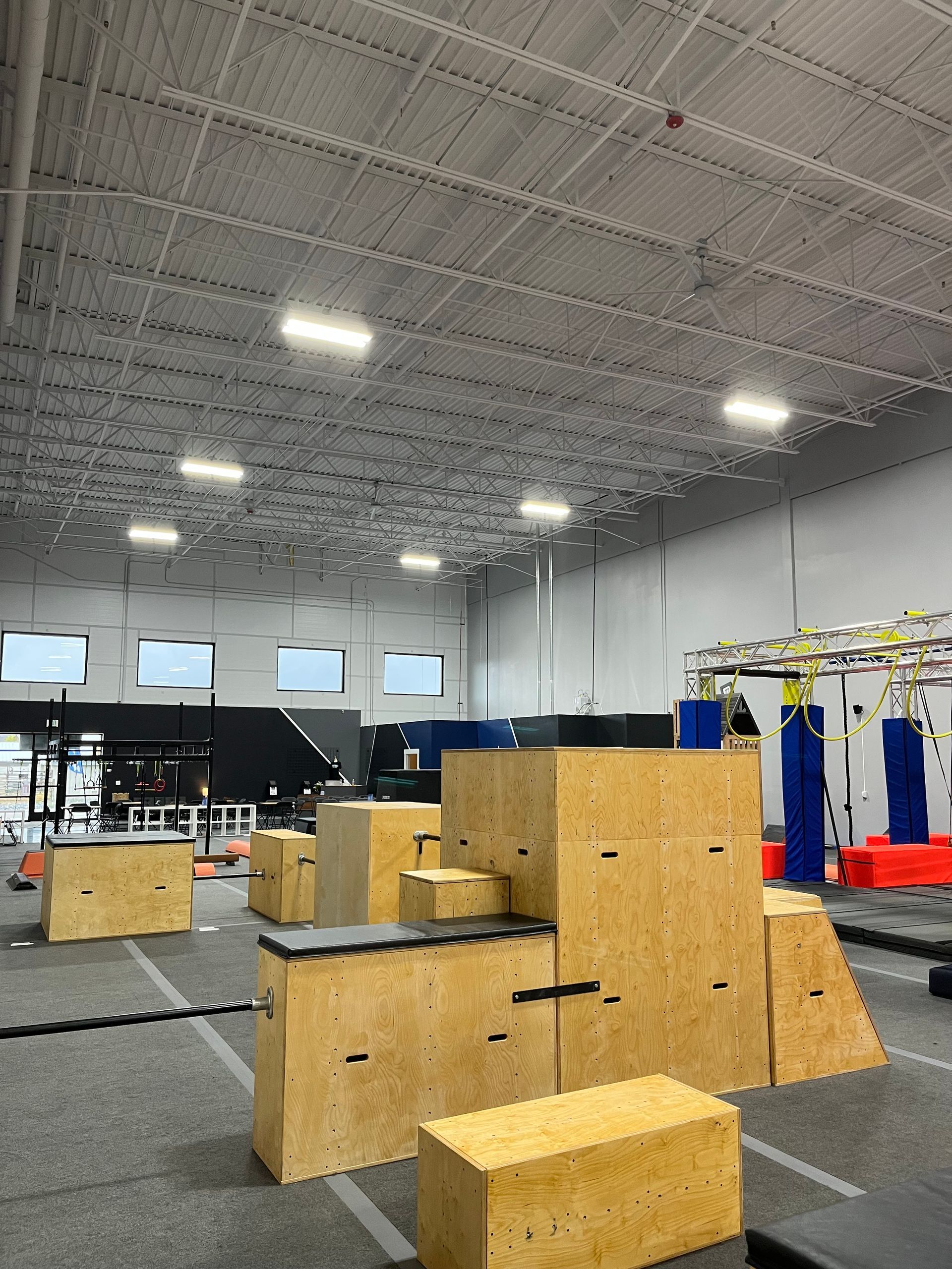 An indoor parkour training facility. Wooden obstacles of various shapes and sizes. Grey floors and white walls.