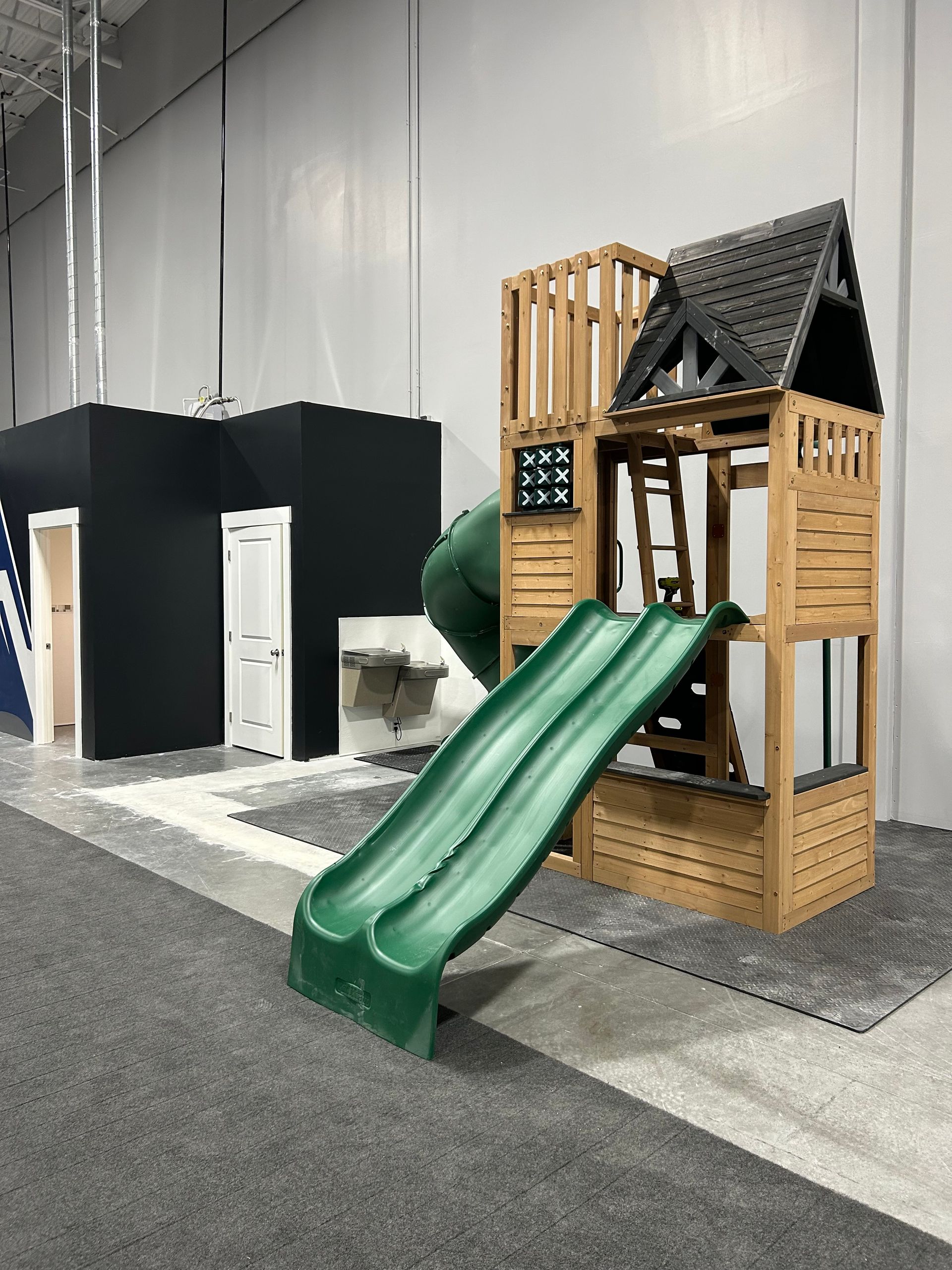 Play structure with green slide, wooden house, and dark blue structure.