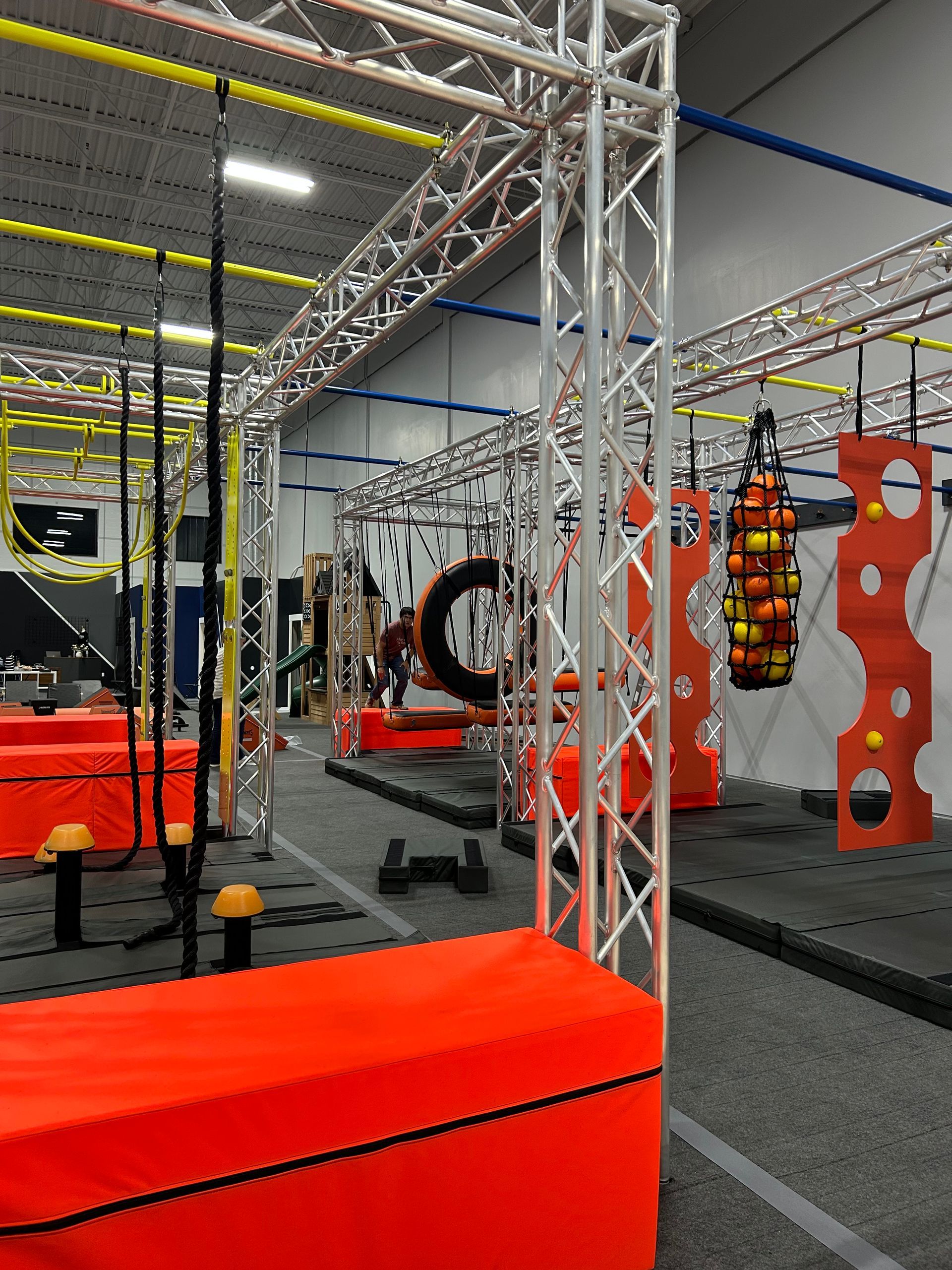 Obstacle course gym with orange and gray structures, ropes, and hanging targets.