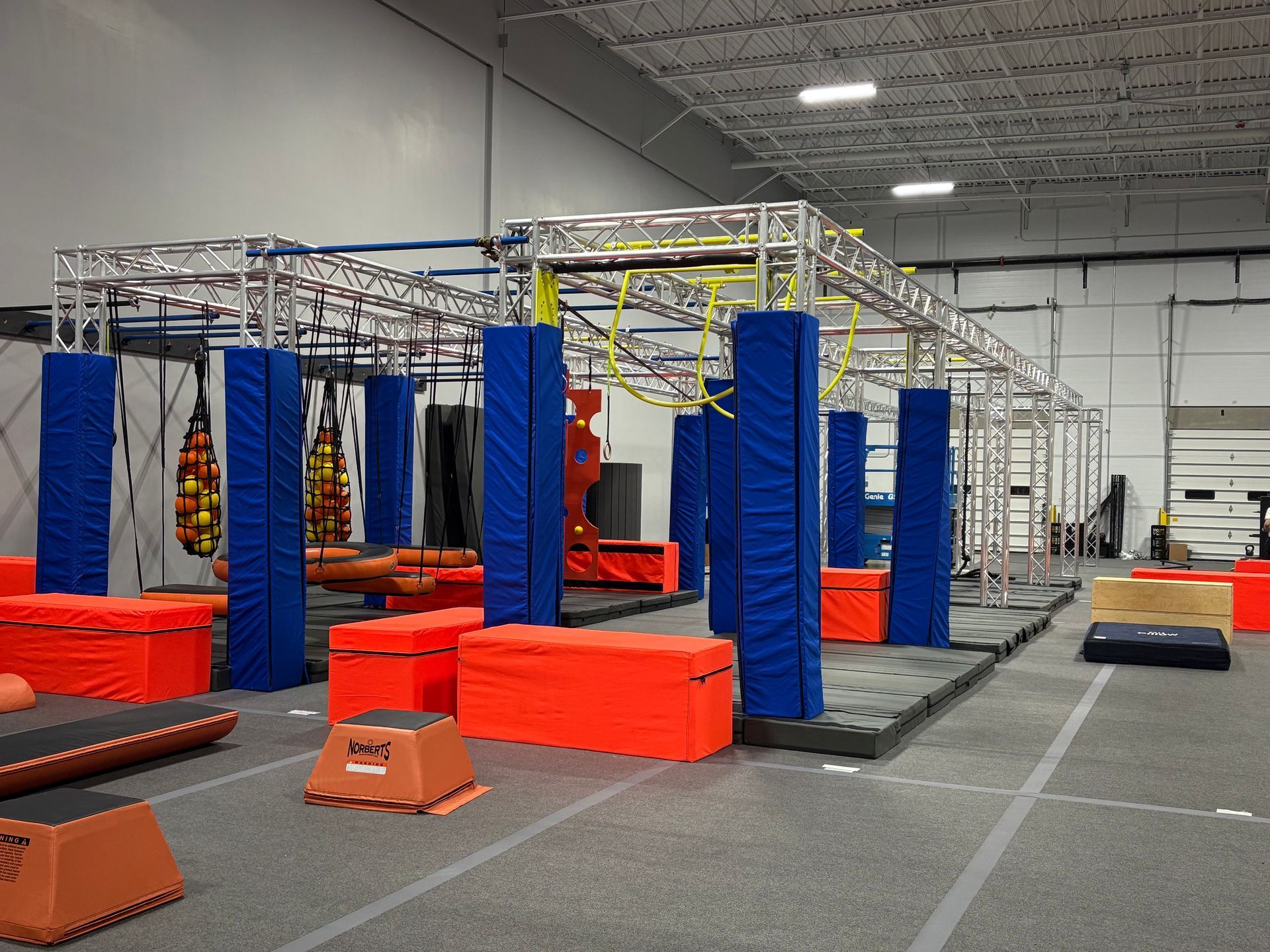 Obstacle course with blue padding and orange blocks in a large indoor gym.