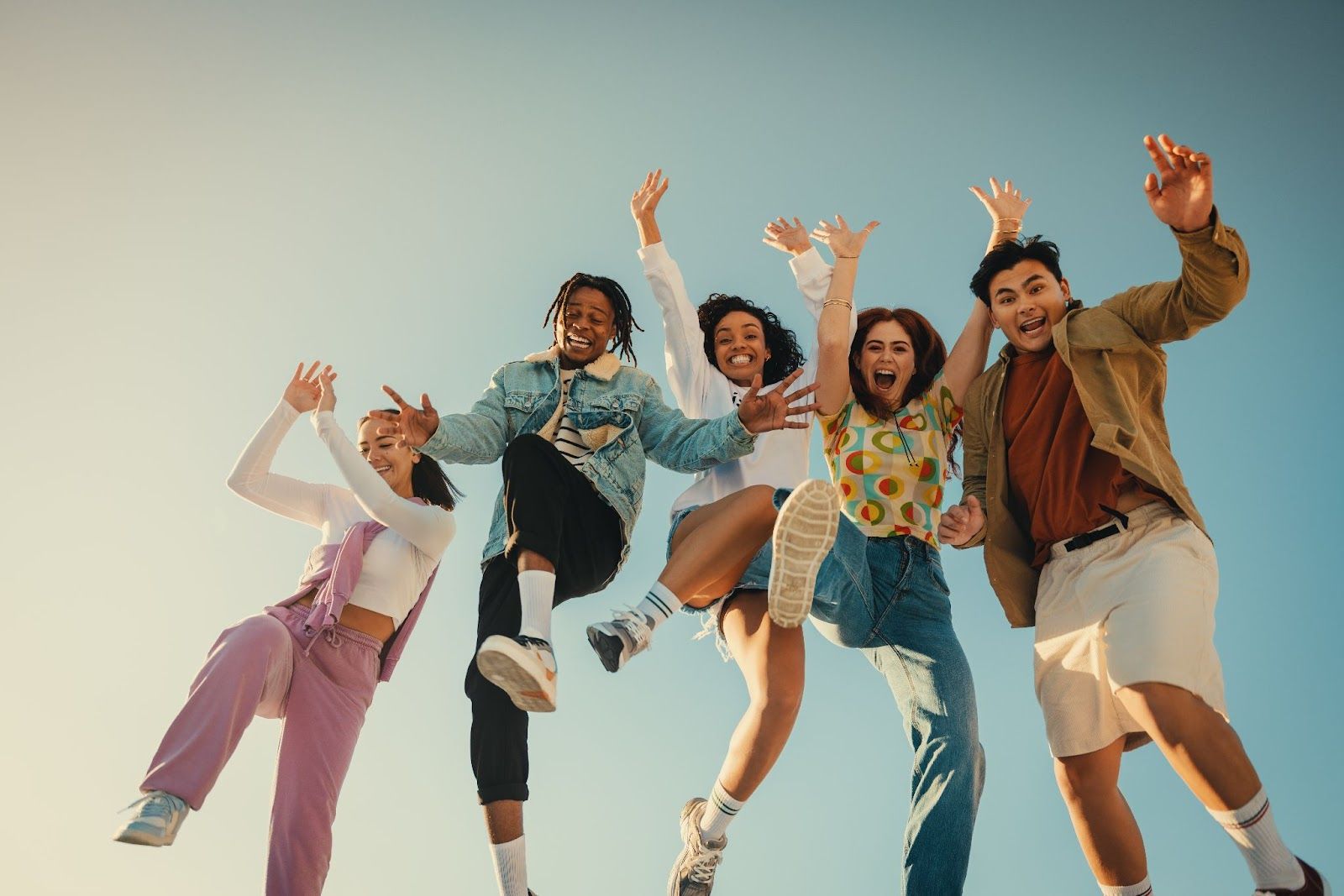 Five people jumping with joy against a blue sky.