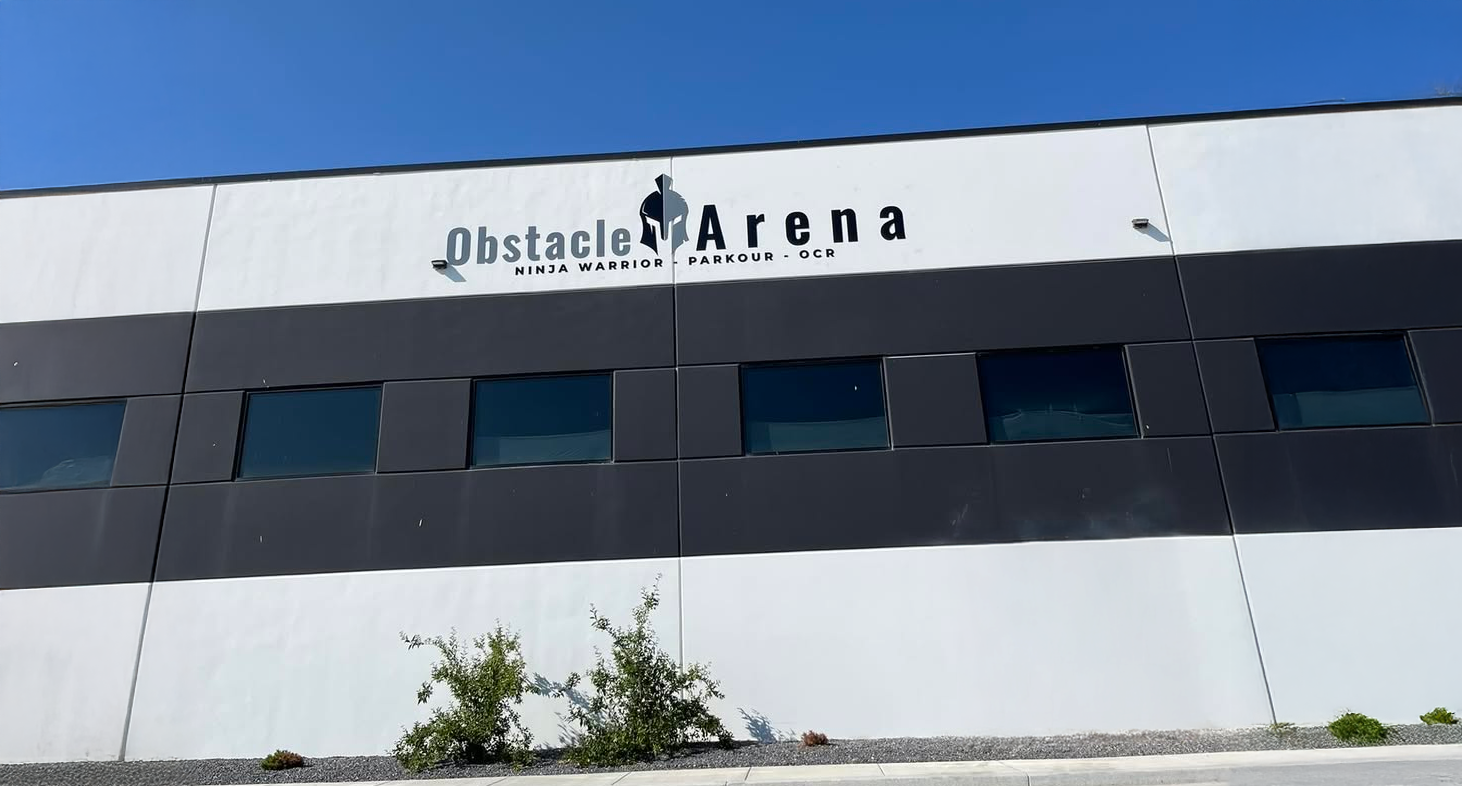 Exterior of Obstacle Arena, a fitness facility. Black and white building, blue sky.
