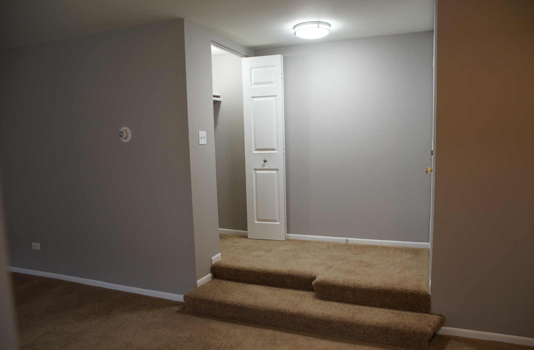 An empty room with stairs leading to a closet and a door.