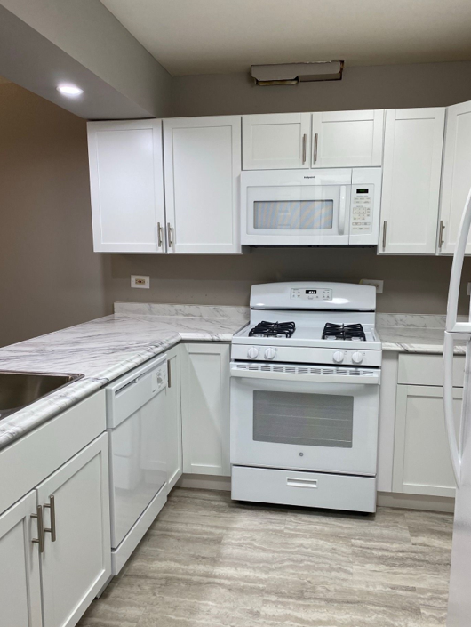 A kitchen with white cabinets and a stove and microwave
