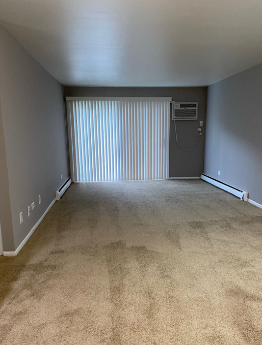An empty living room with a sliding glass door and a window.