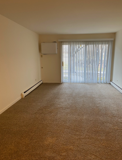 An empty living room with a sliding glass door and blinds.