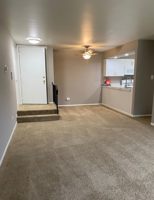 An empty living room with a ceiling fan and stairs