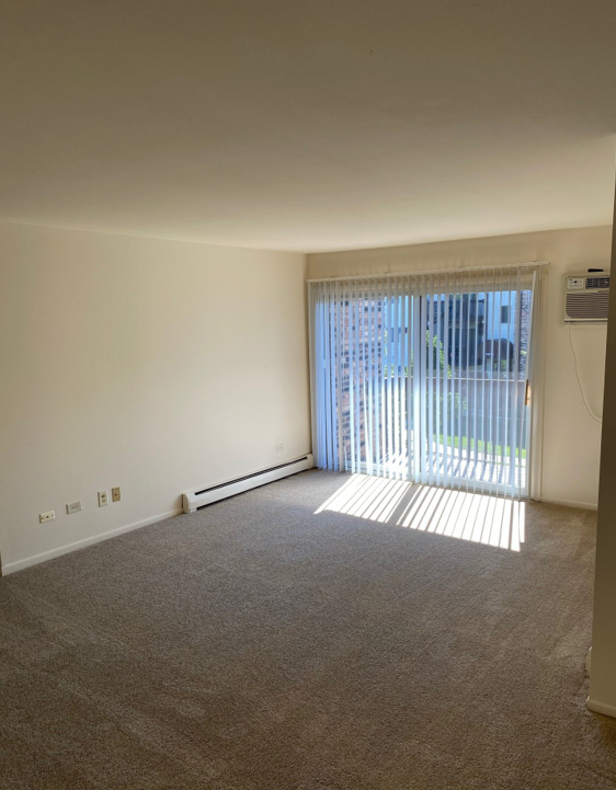 An empty living room with a sliding glass door and blinds.