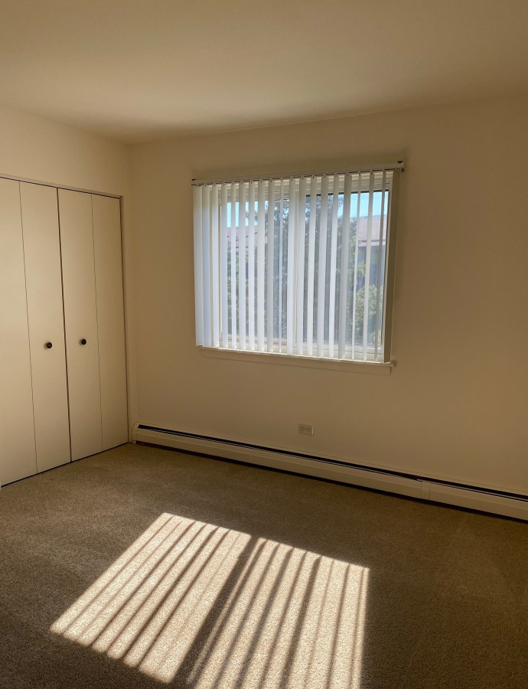 An empty bedroom with a window and blinds.