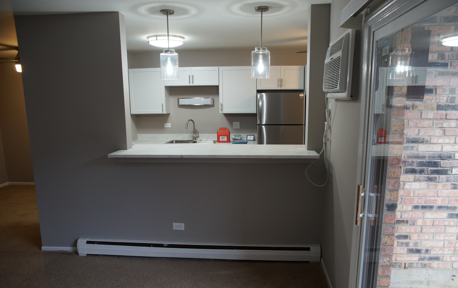 An empty kitchen with white cabinets and a stainless steel refrigerator