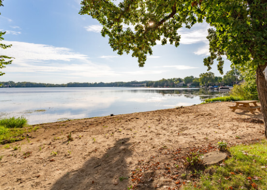 A sandy beach next to a lake with a picnic table.