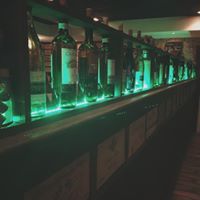 Liquor bottles on a shelf with green LED lighting, in a dimly lit bar.