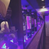 Bottles of wine lined up on a shelf with purple neon lighting.