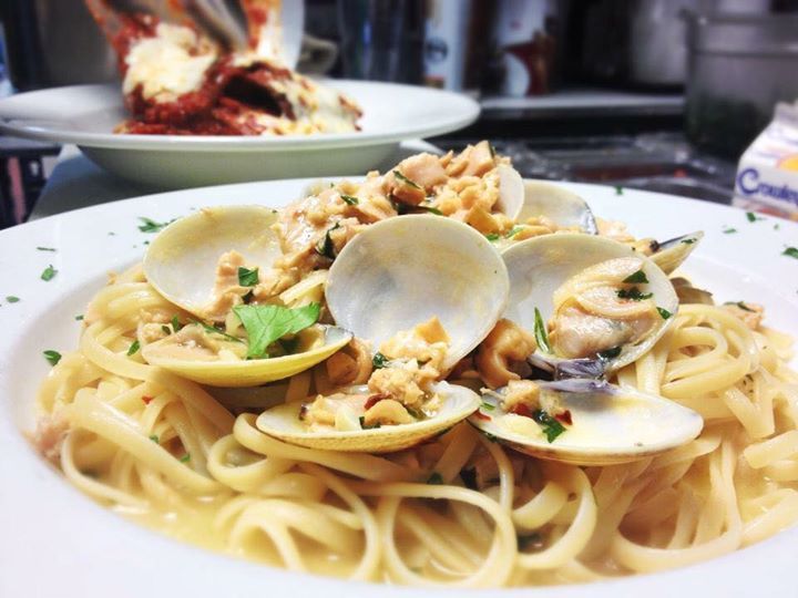 Linguine with clams, garnished with parsley, on a white plate. Another dish is out of focus in the background.