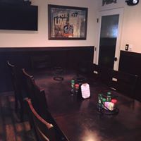 A dark wooden table with chairs. A framed sign and a television hang on the wall.