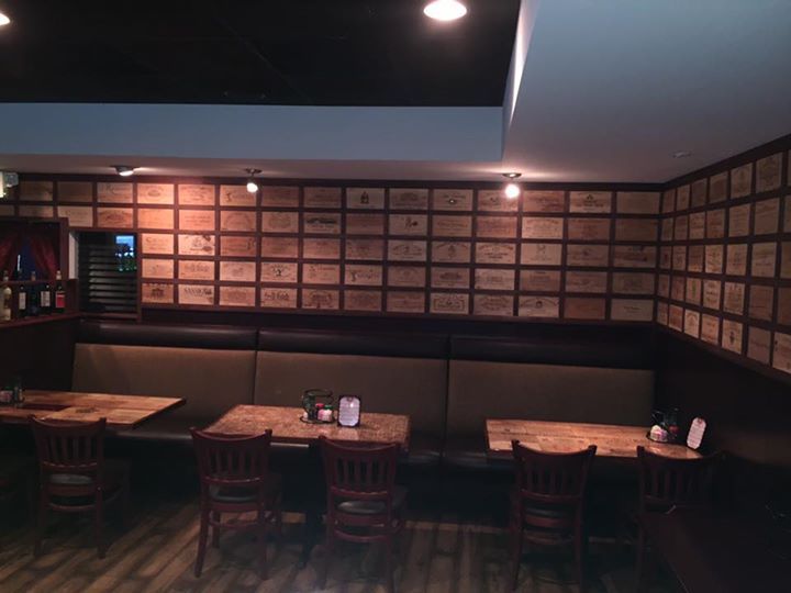 Restaurant interior with wooden tables, dark brown chairs, booths, and a wall decorated with wooden boxes.