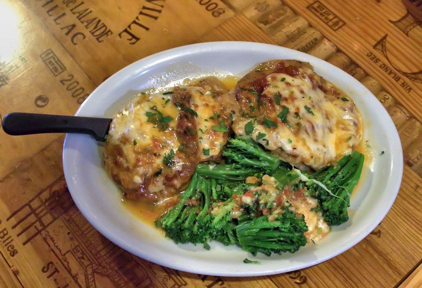 Chicken parmesan with broccoli on a white plate, served on a wooden table.