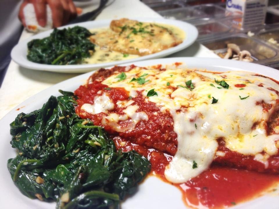 Two plates of Italian food, one with chicken and sauce, the other with red sauce and cheese, both with sauteed spinach.