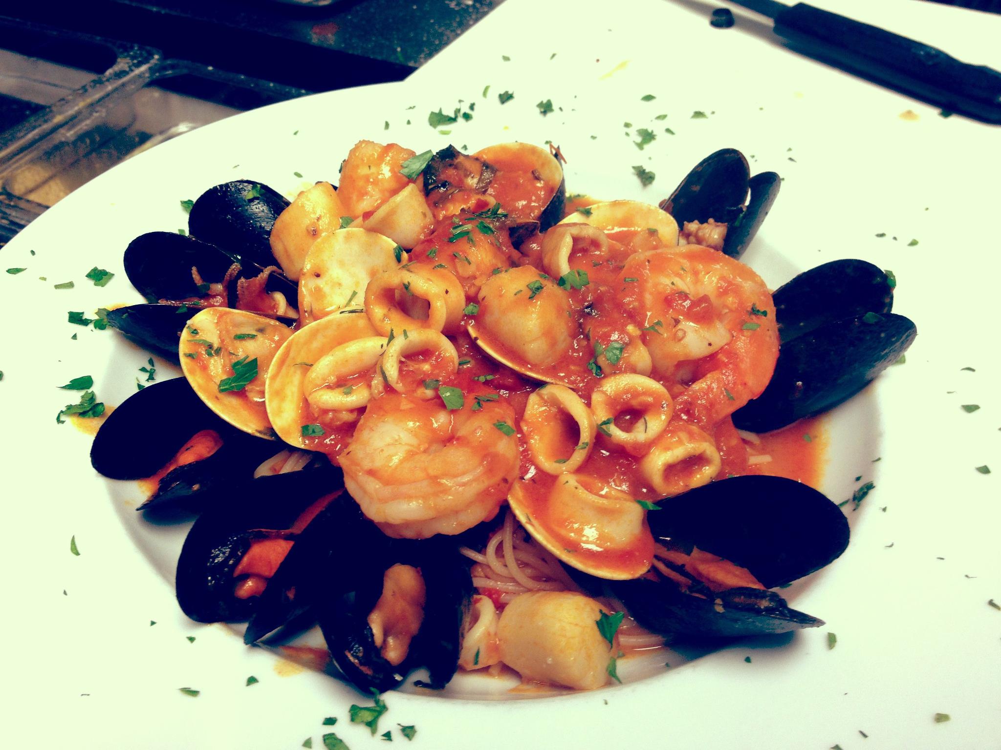 Seafood pasta dish: mussels, shrimp, clams, calamari, and sauce on a white plate.