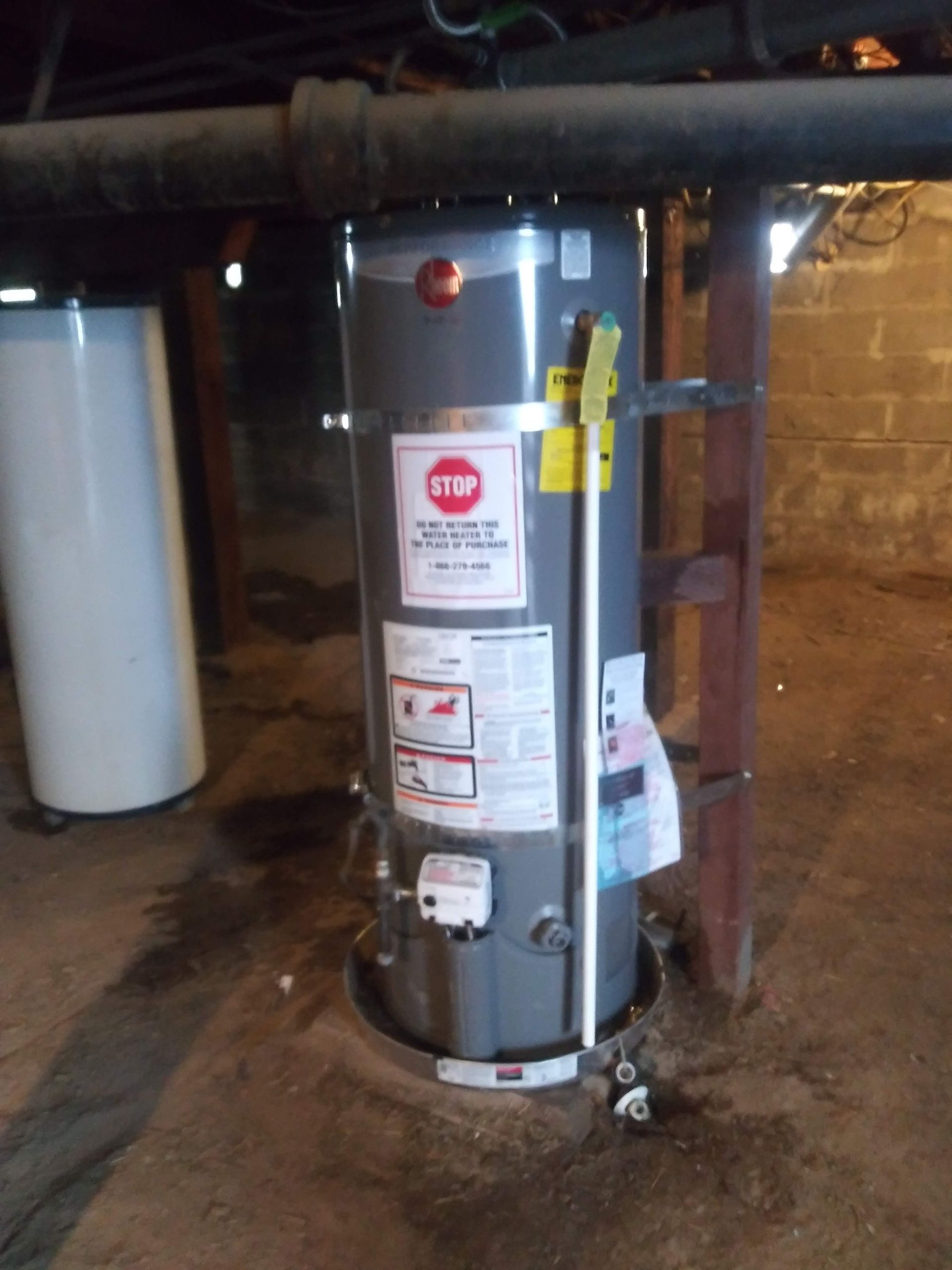 A new water heater in a basement; gray tank, white pipes, and safety labels are visible.