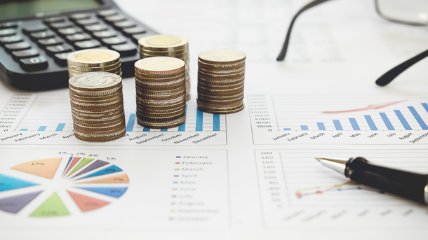 Stacks of coins, calculator, glasses, and pen on financial reports with graphs.