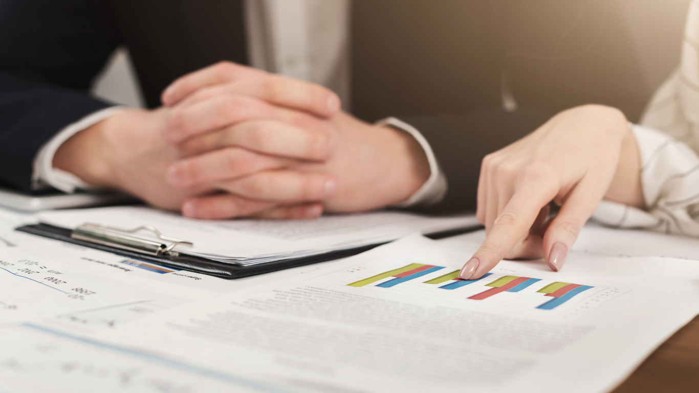 Hands pointing at a bar graph on a document during a meeting.