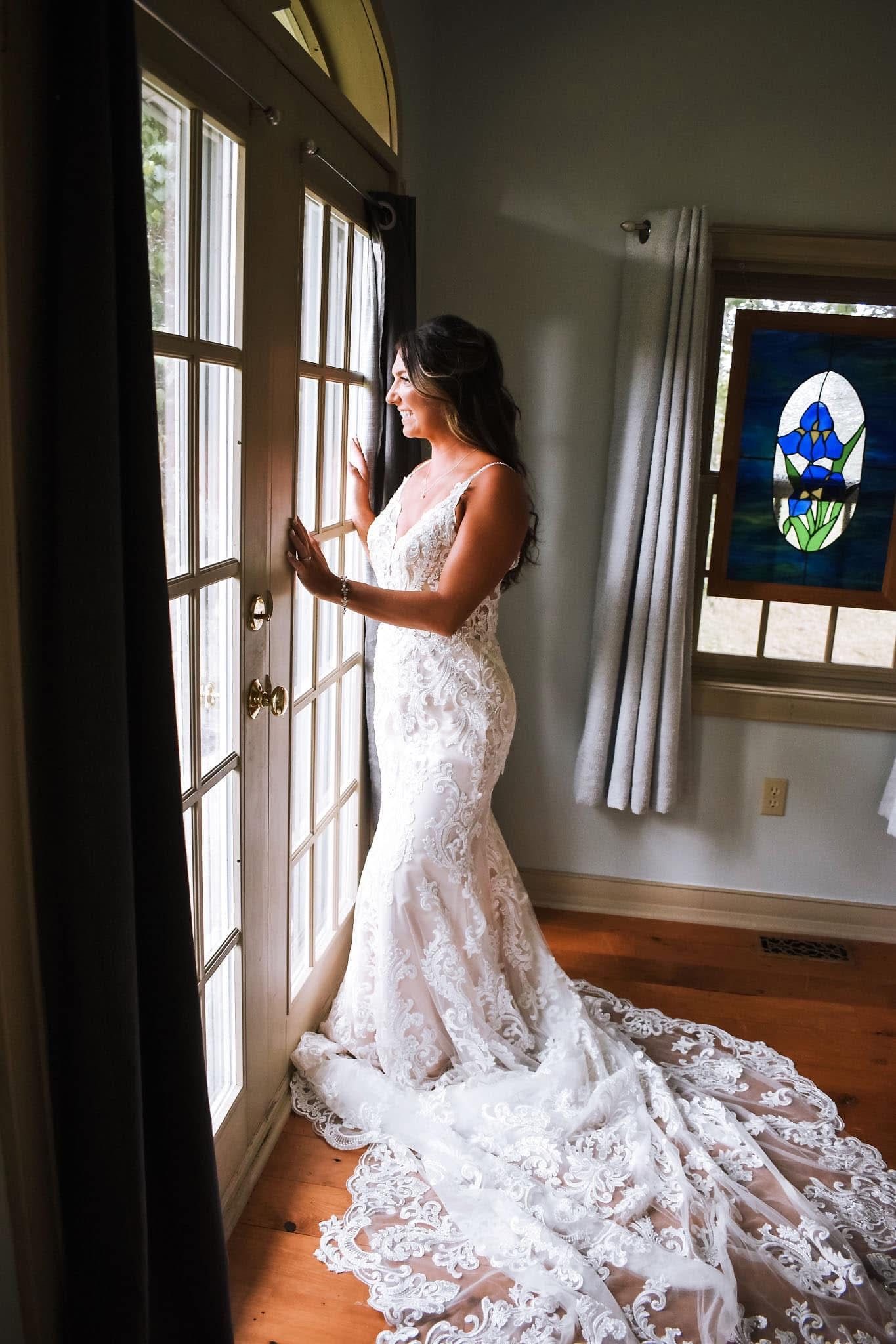 A woman in a wedding dress is standing in front of a window.