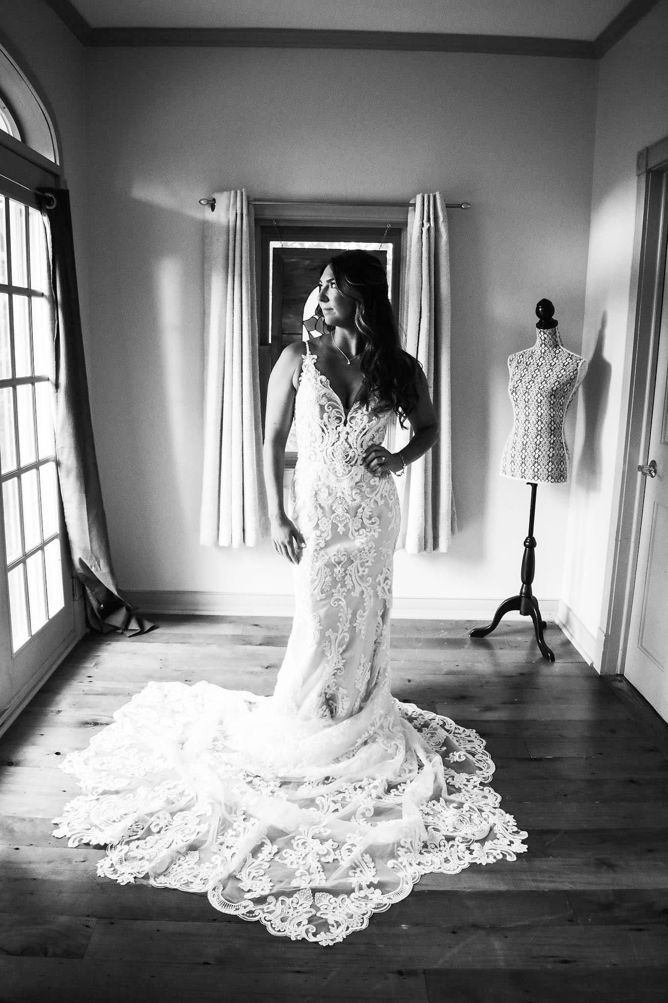A black and white photo of a bride in a wedding dress standing in a room.