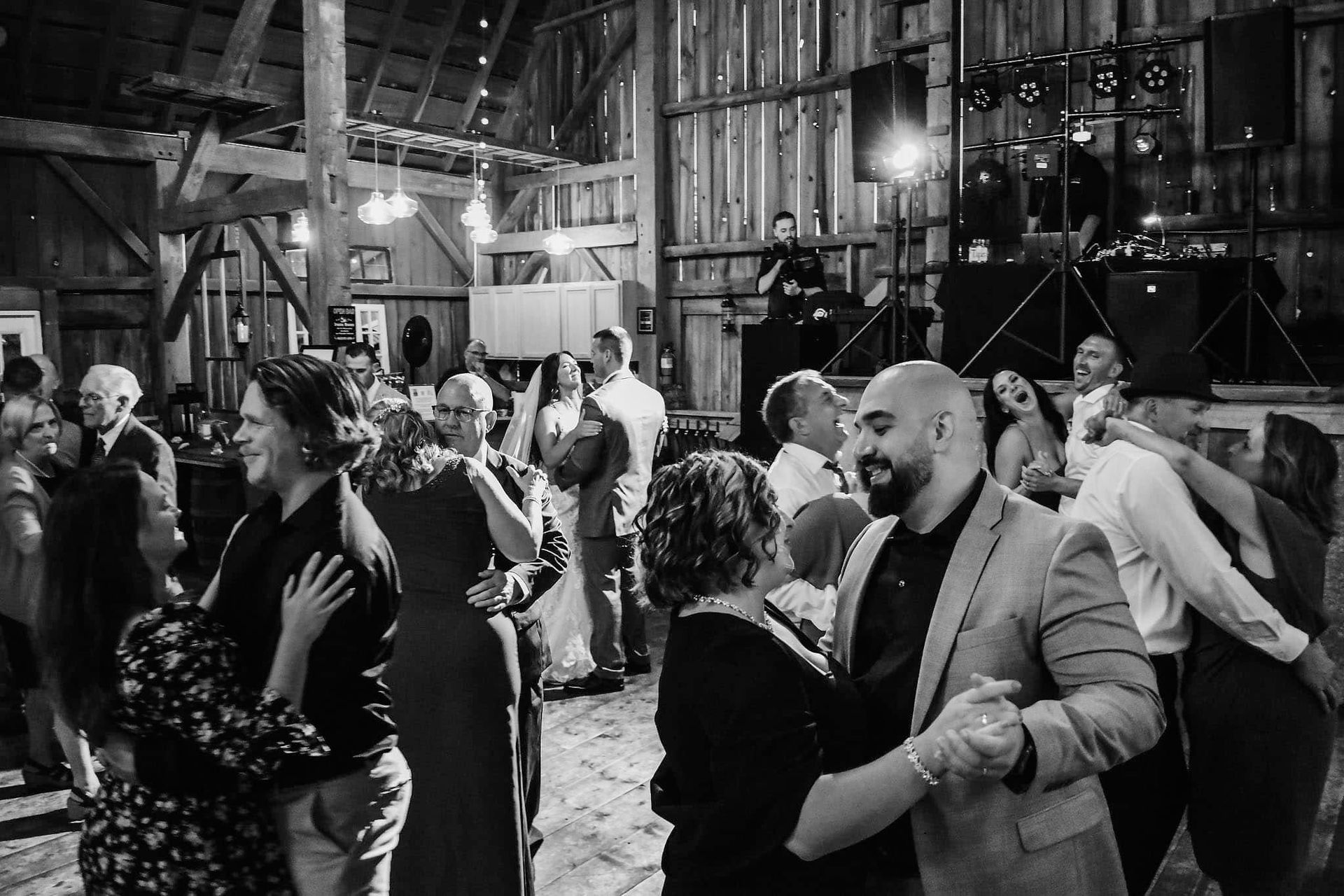 A group of people are dancing in a barn at a wedding reception.