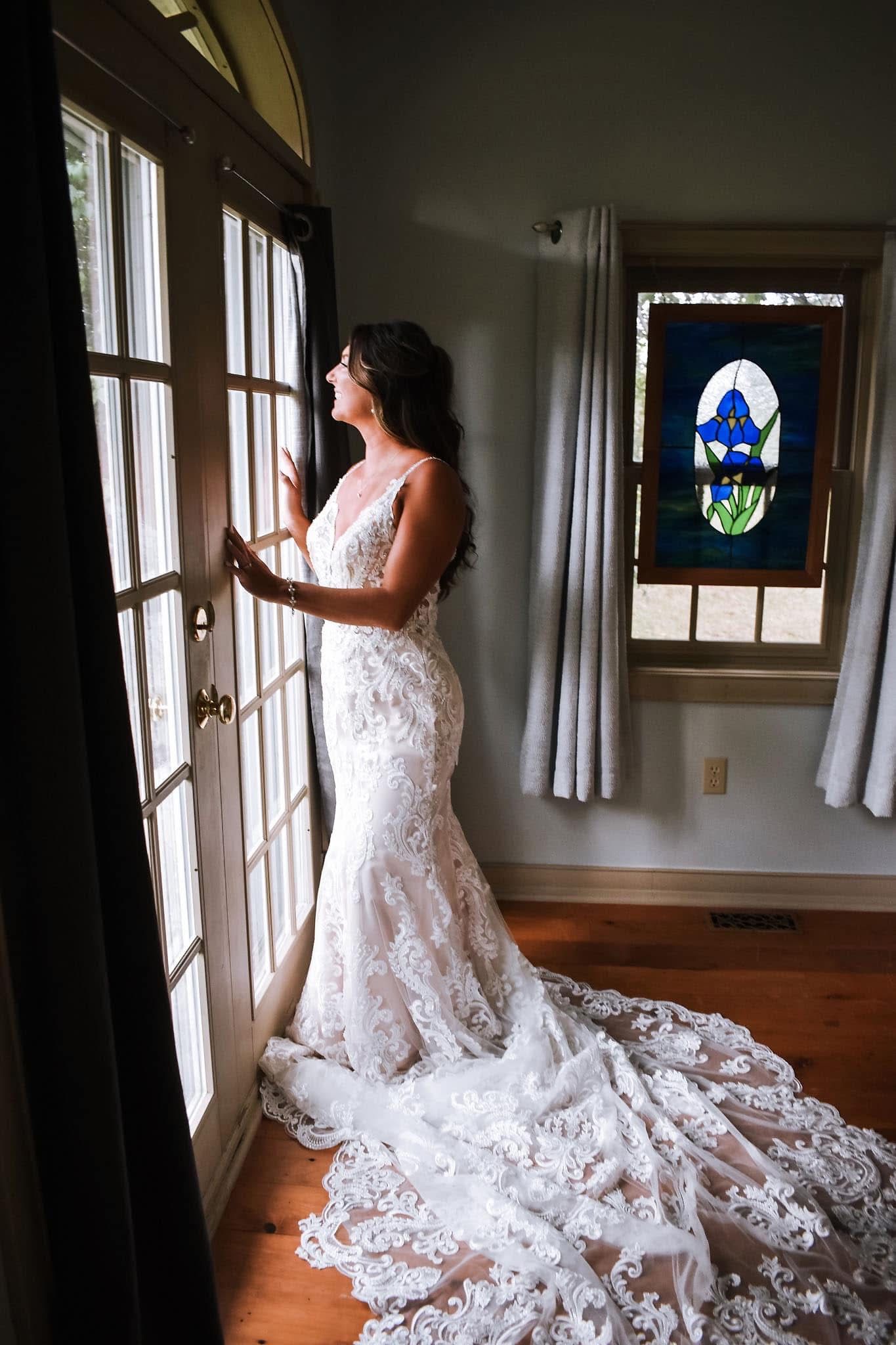 A woman in a wedding dress is standing in front of a window.