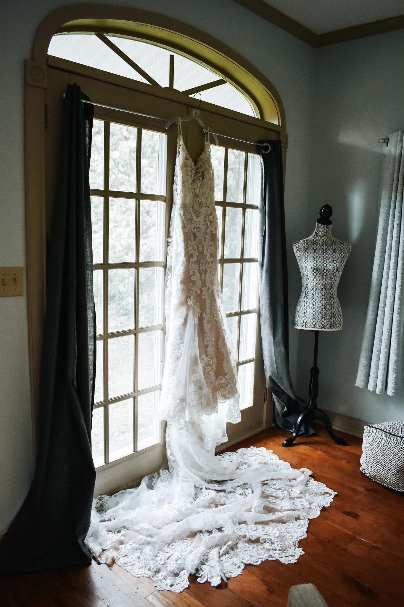 A wedding dress is hanging in a window next to a mannequin.