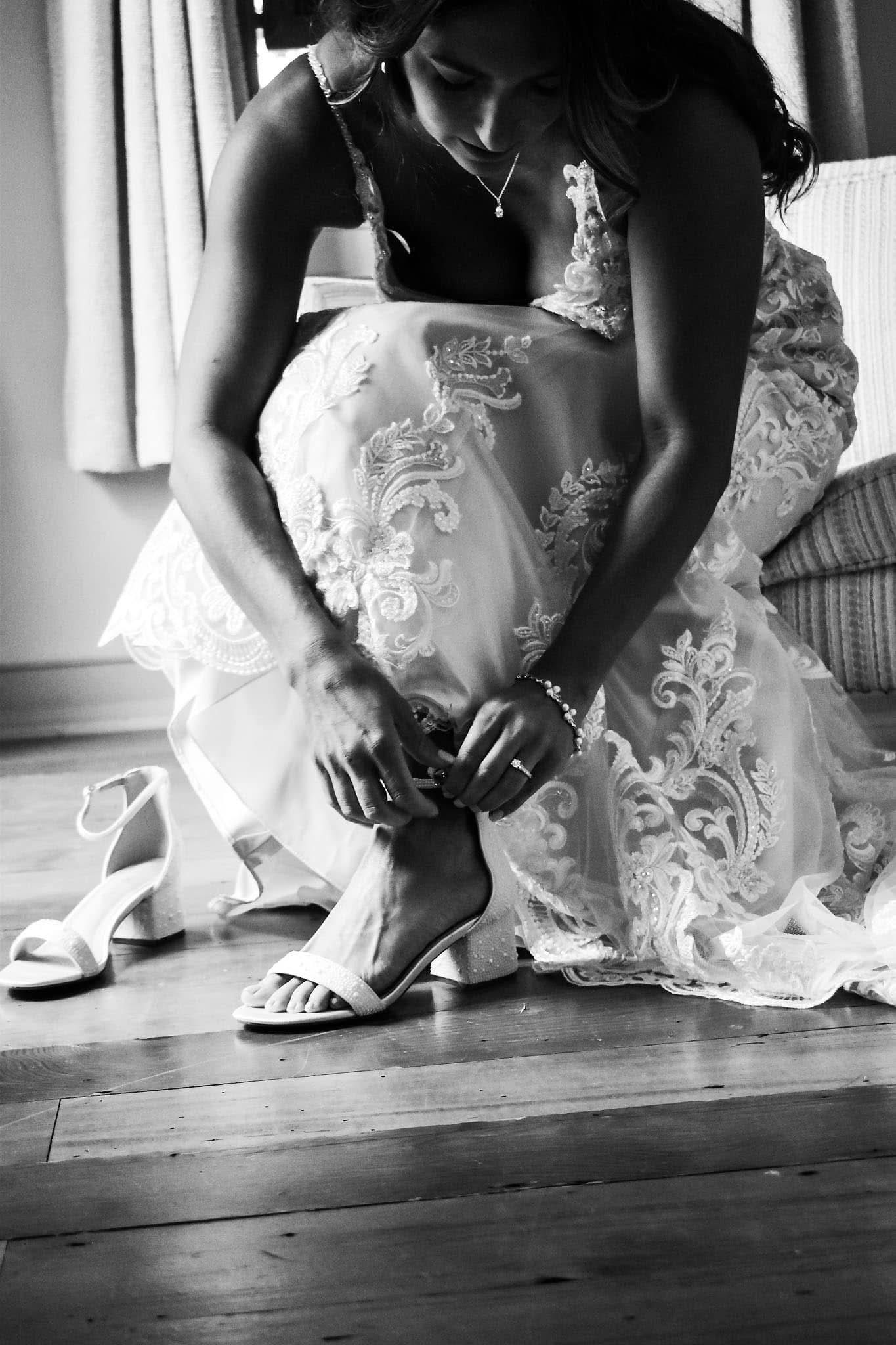 A woman in a wedding dress is tying her shoes in a black and white photo.