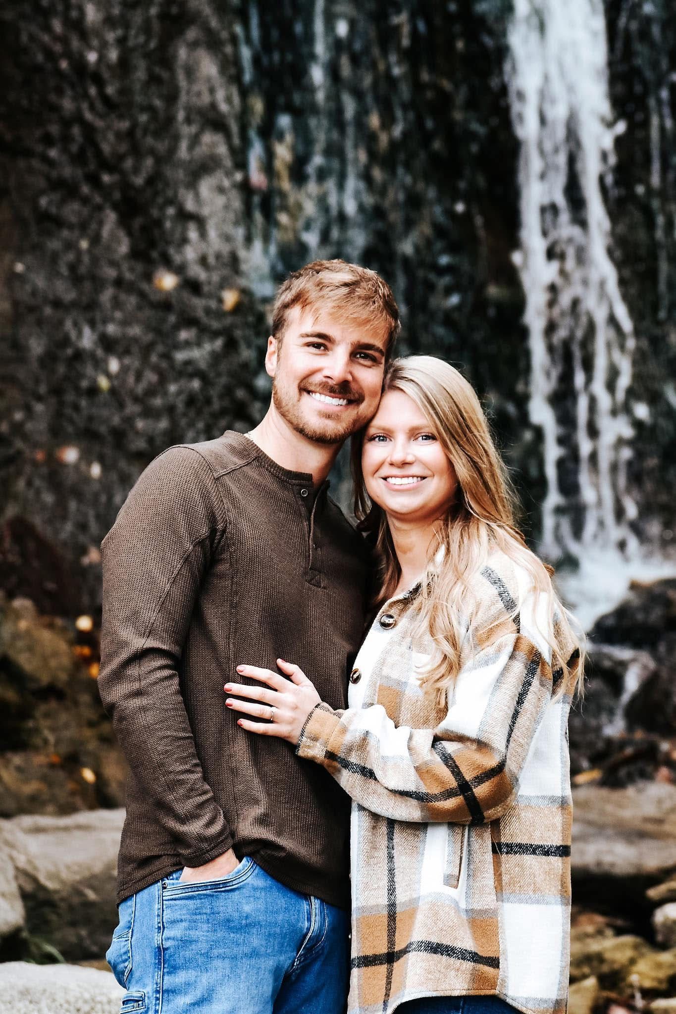 A man and a woman are posing for a picture in front of a waterfall.