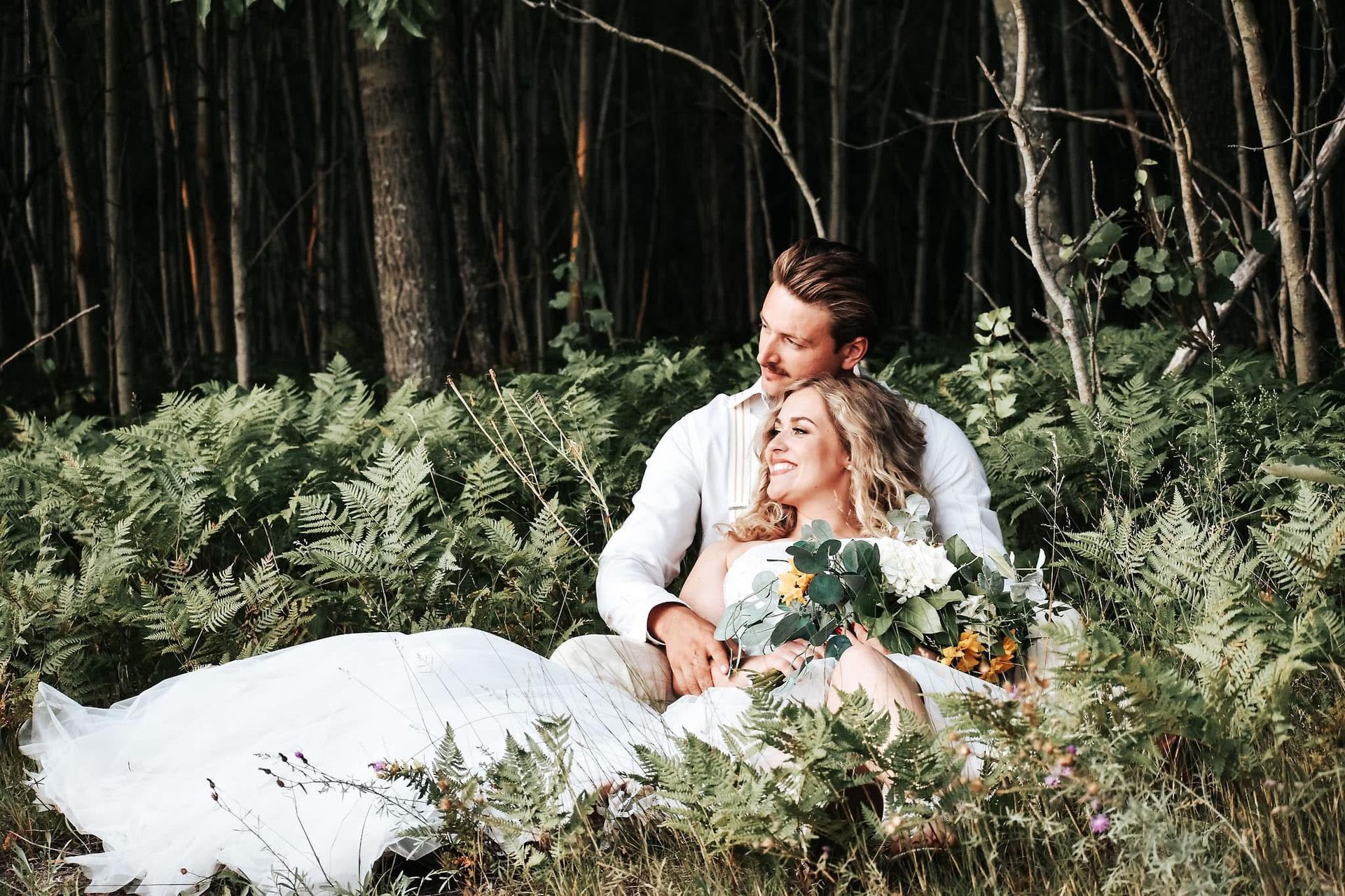 A bride and groom are sitting in the middle of a forest.
