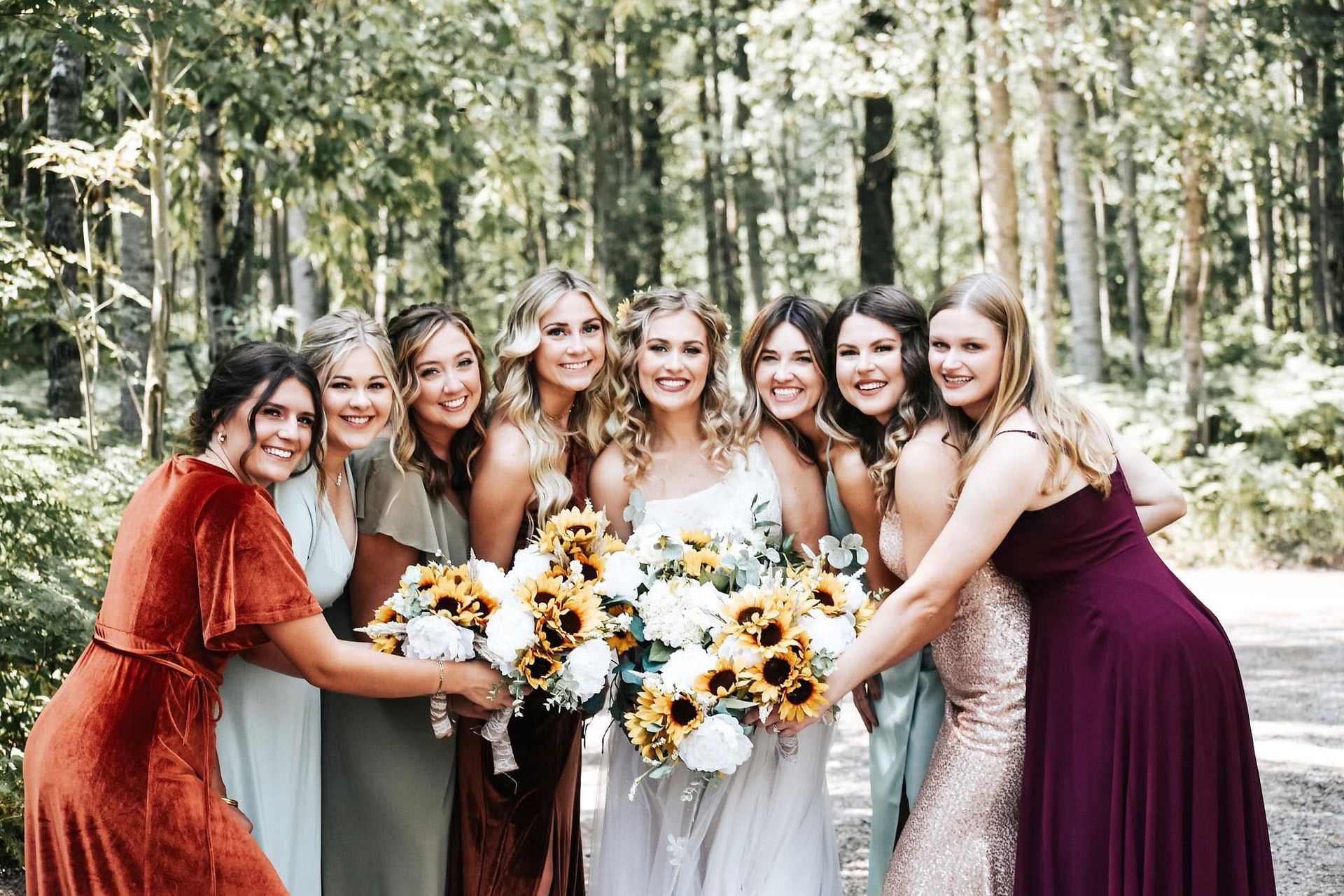 A bride and her bridesmaids are posing for a picture in the woods.