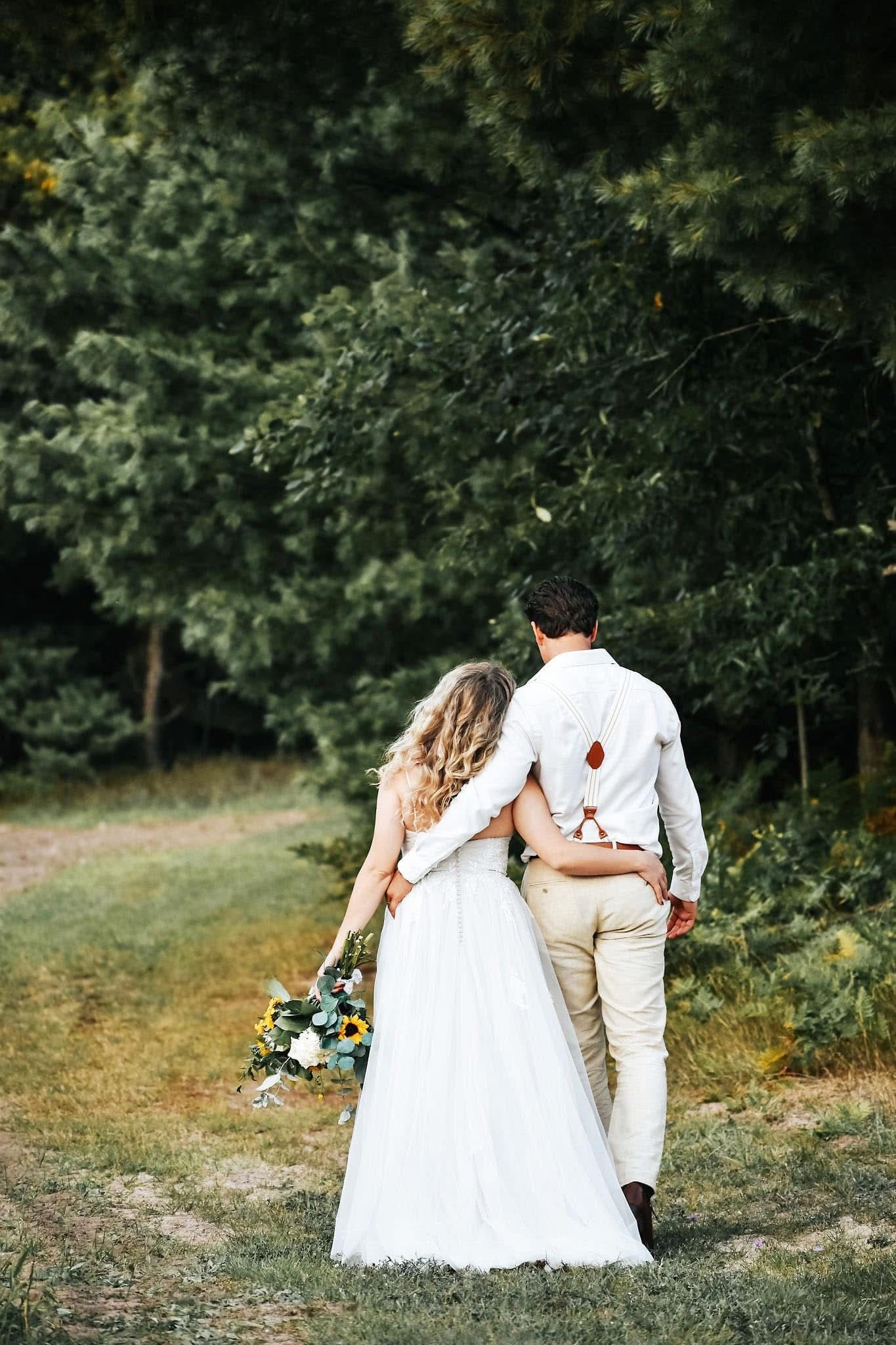 A bride and groom are walking down a path in the woods.