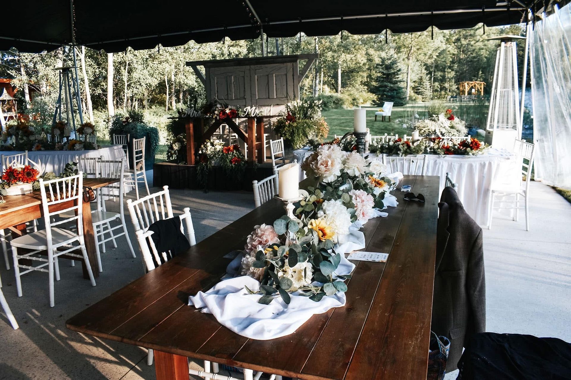 A long wooden table with flowers on it is under a tent.