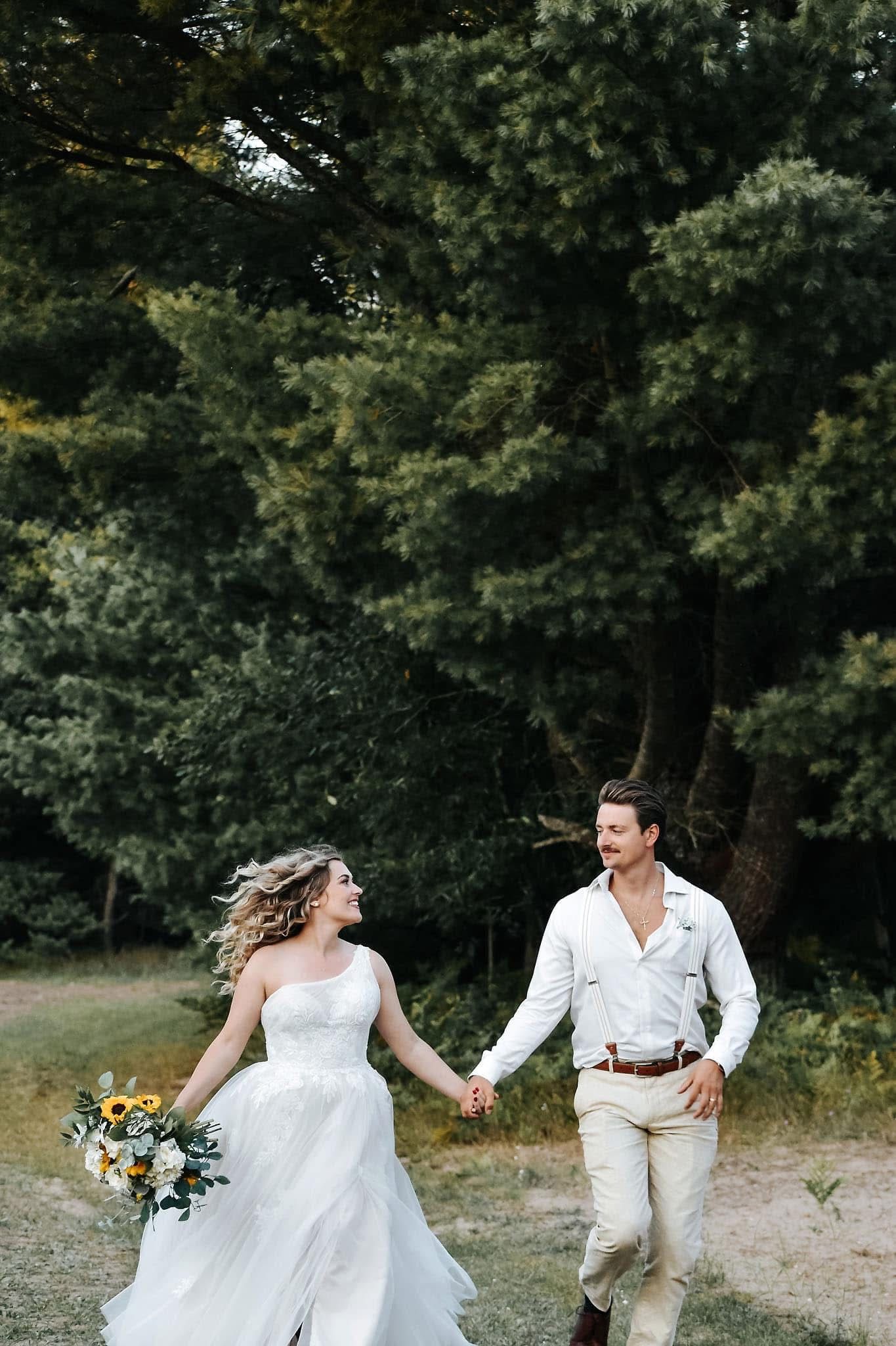 A bride and groom are holding hands and running through a field.
