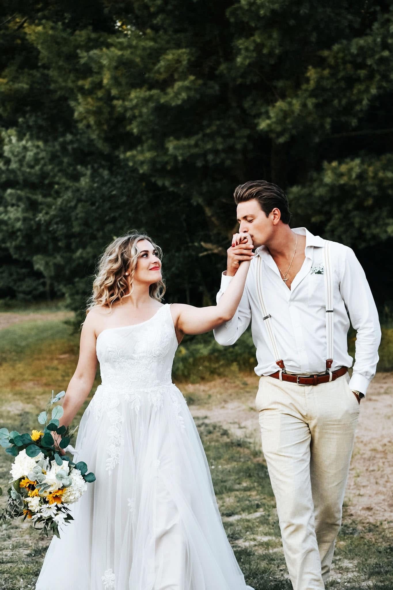 A bride and groom are walking through a field holding hands.