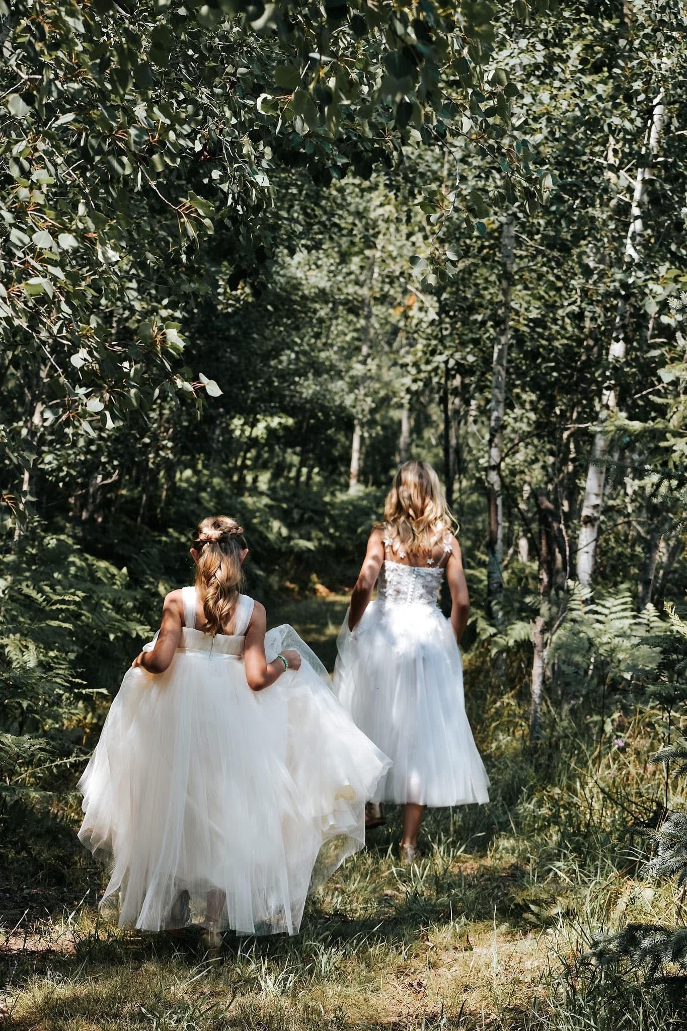 Two women in white dresses are walking through a forest.