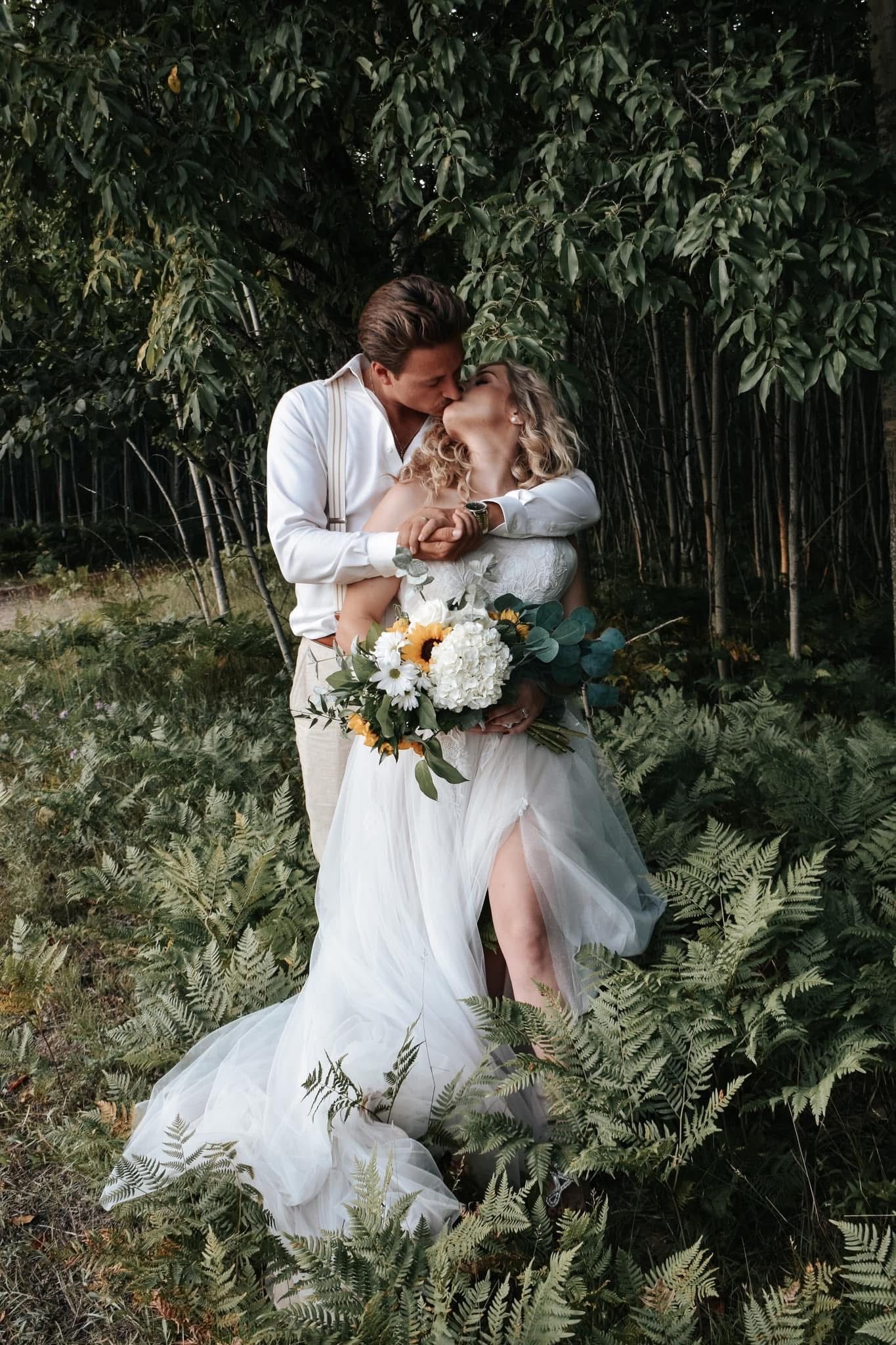 A bride and groom are kissing in a field of ferns.