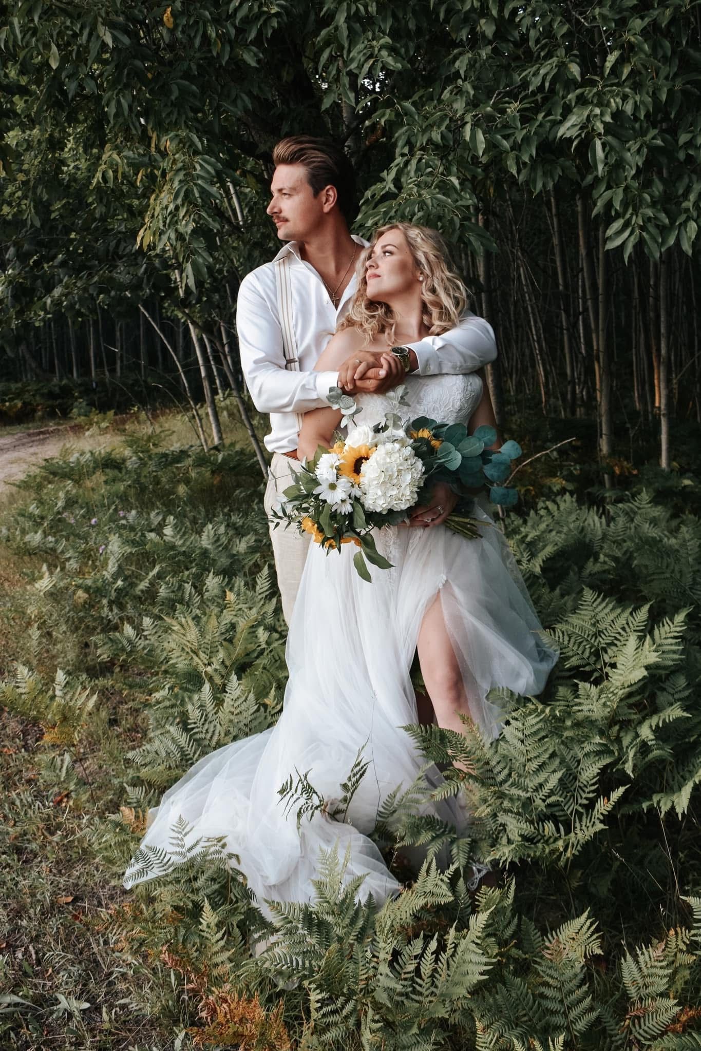 A bride and groom are posing for a picture in the woods.