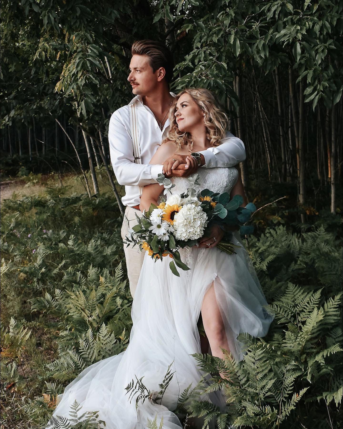 A bride and groom are posing for a picture in the woods.