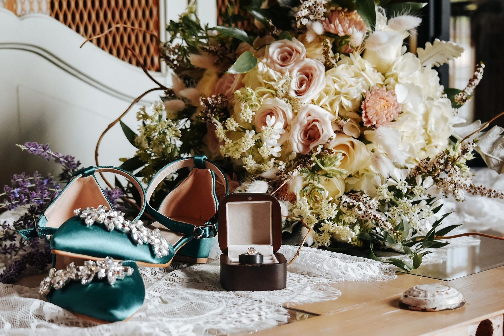 A bride 's wedding shoes , rings , and bouquet of flowers are on a table.