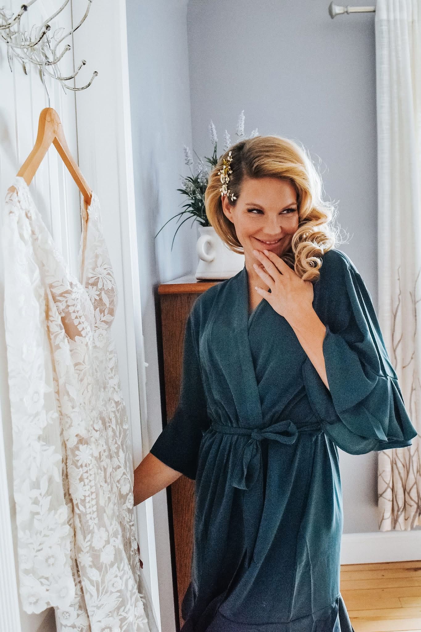 A woman in a robe is standing next to a wedding dress.