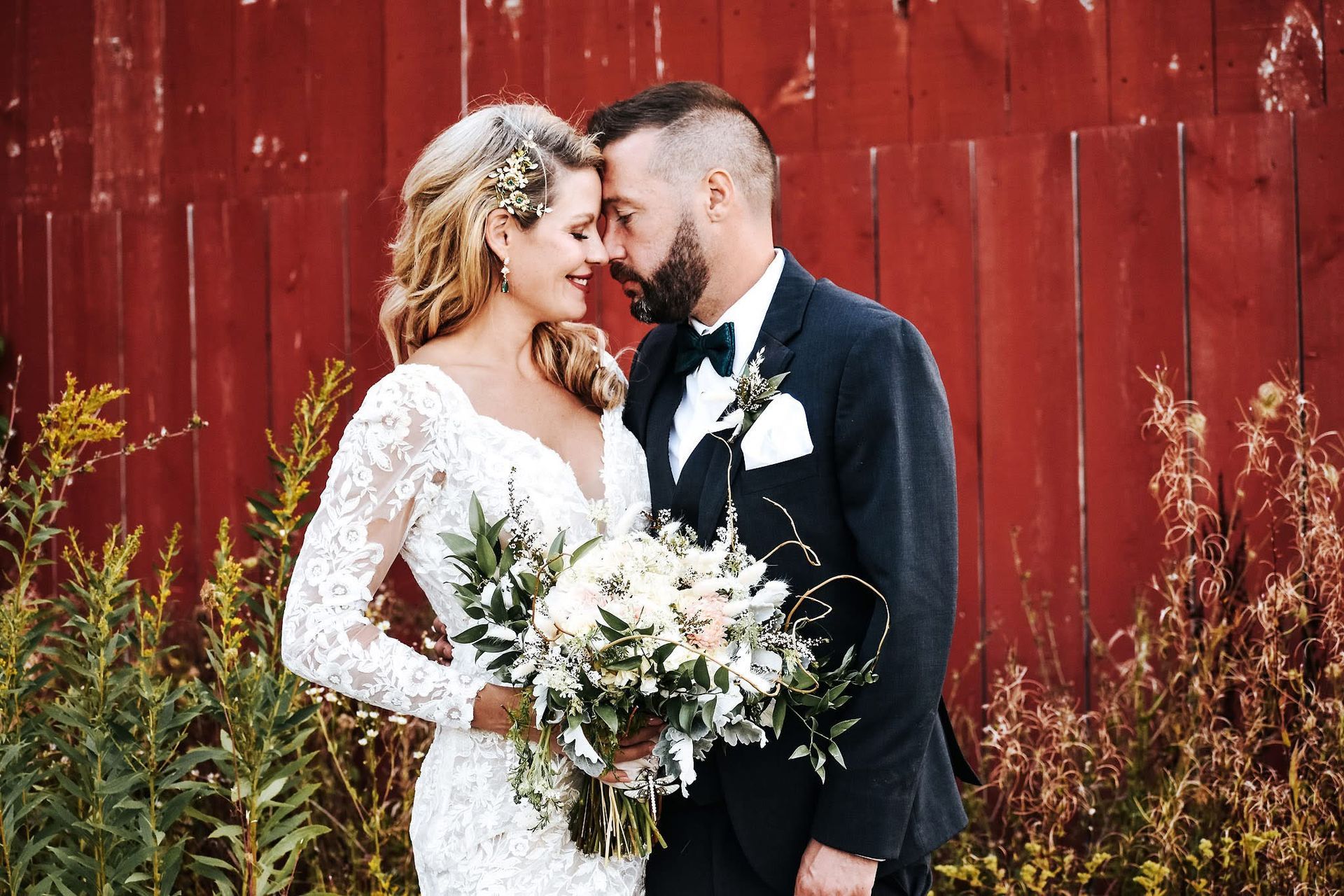 A bride and groom are posing for a picture in front of a red barn.